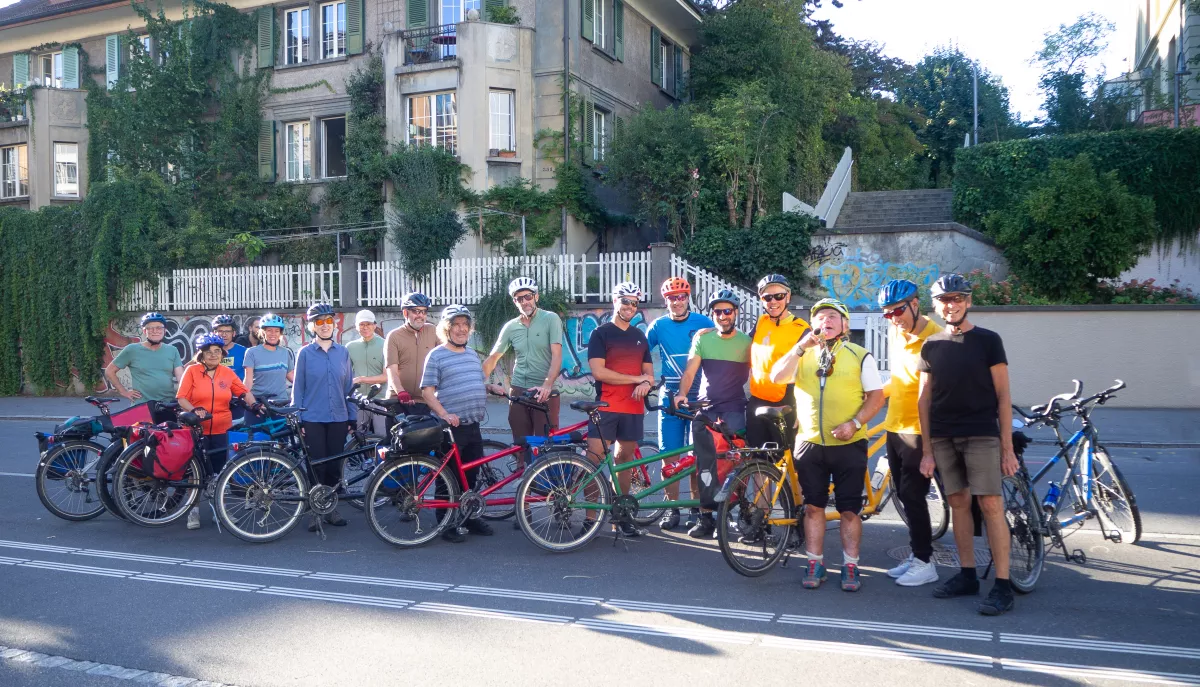 Eine Gruppe Menschen mit Fahrrädern vor einem Wohngebäude die in die Kamera lachen.